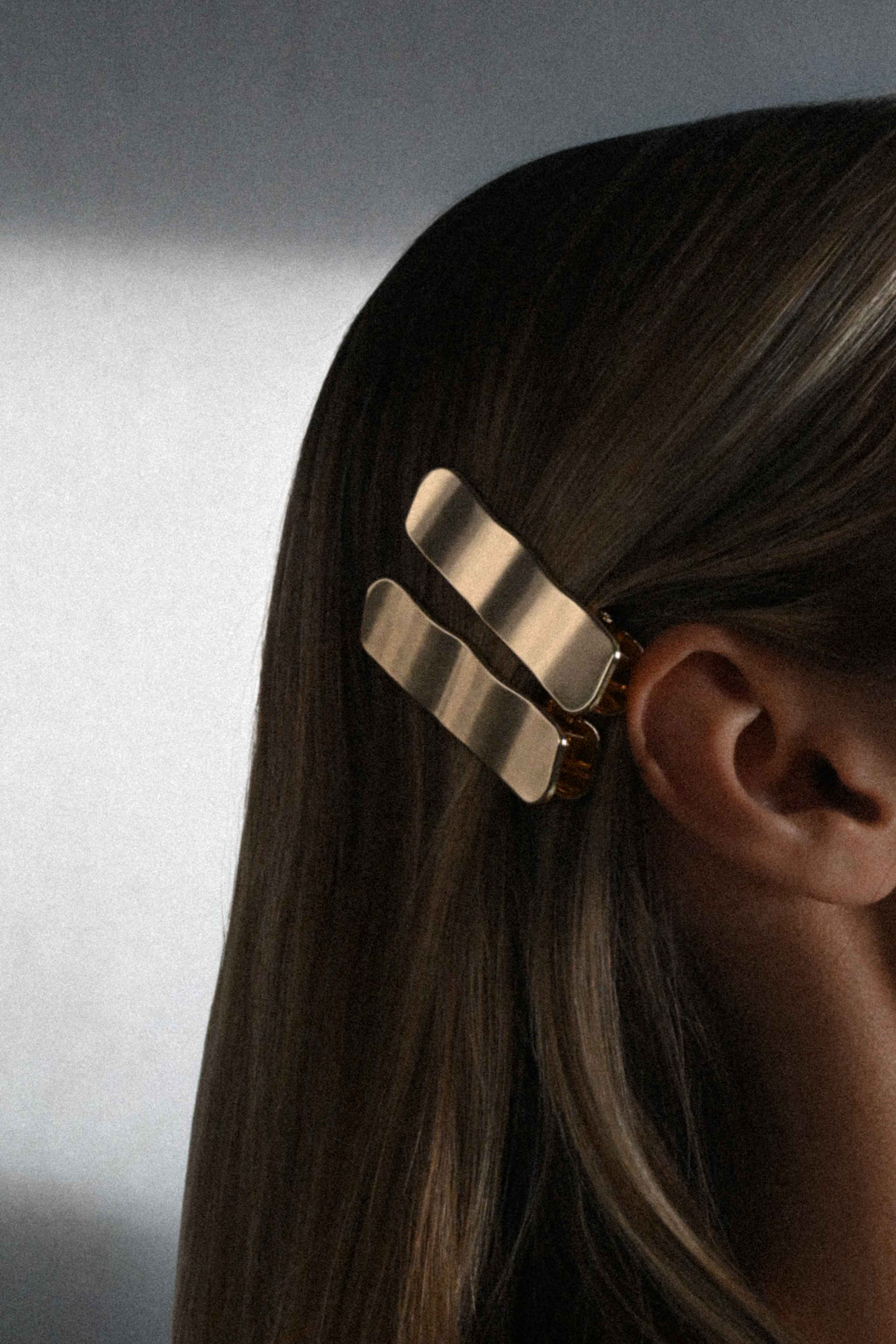 Gold hair clip on a person's hair against a neutral background