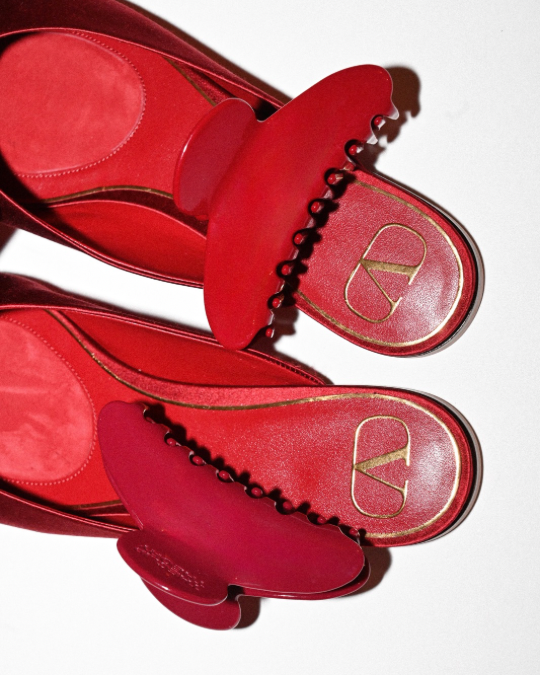 Red sandals with a gold logo on a white background with two red hair clips