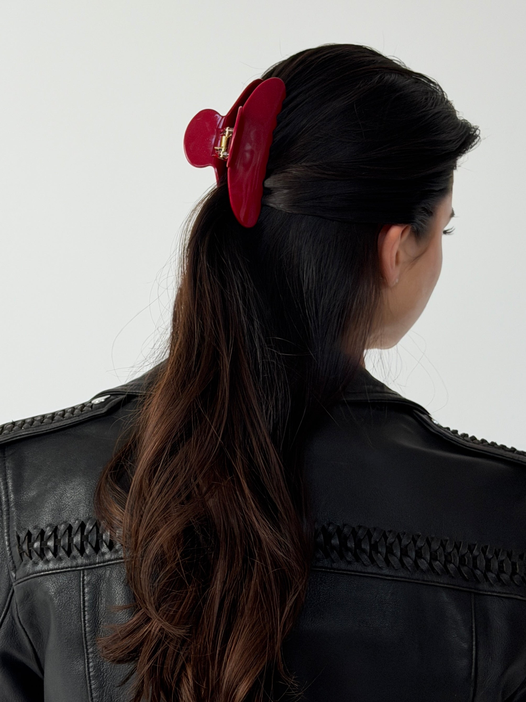 Person with a red hair clip in their dark hair wearing a black leather jacket on a white background