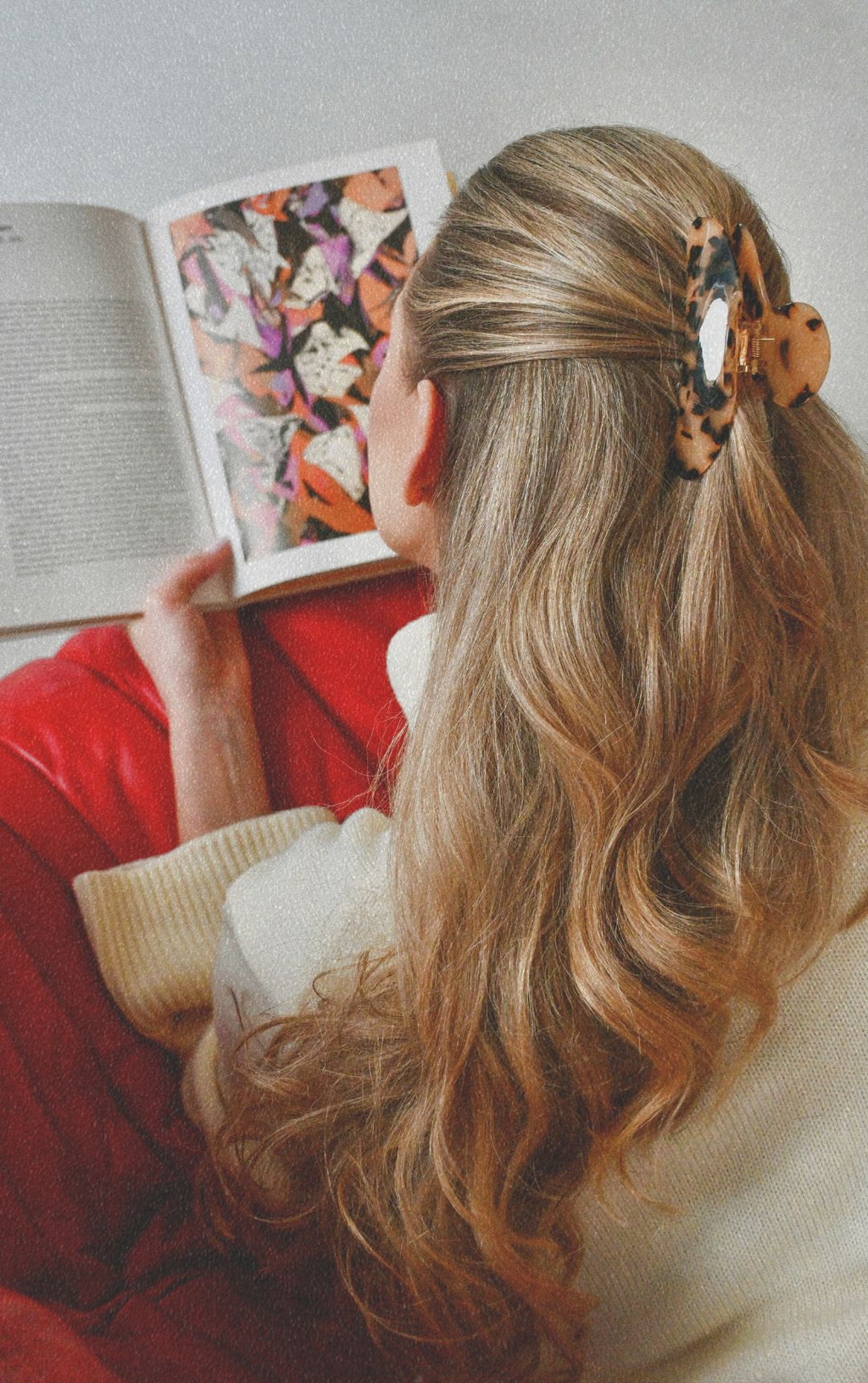 Person with long blonde hair wearing a leopard print hair clip, reading a book.